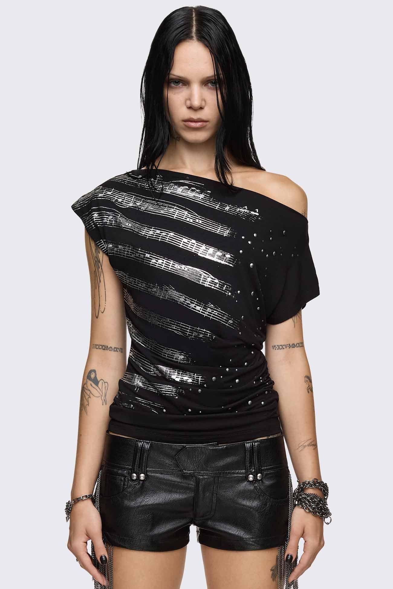 Black off shoulder top with silver sheet music graphic, silver studs, asymmetrical neckline and ruched side.