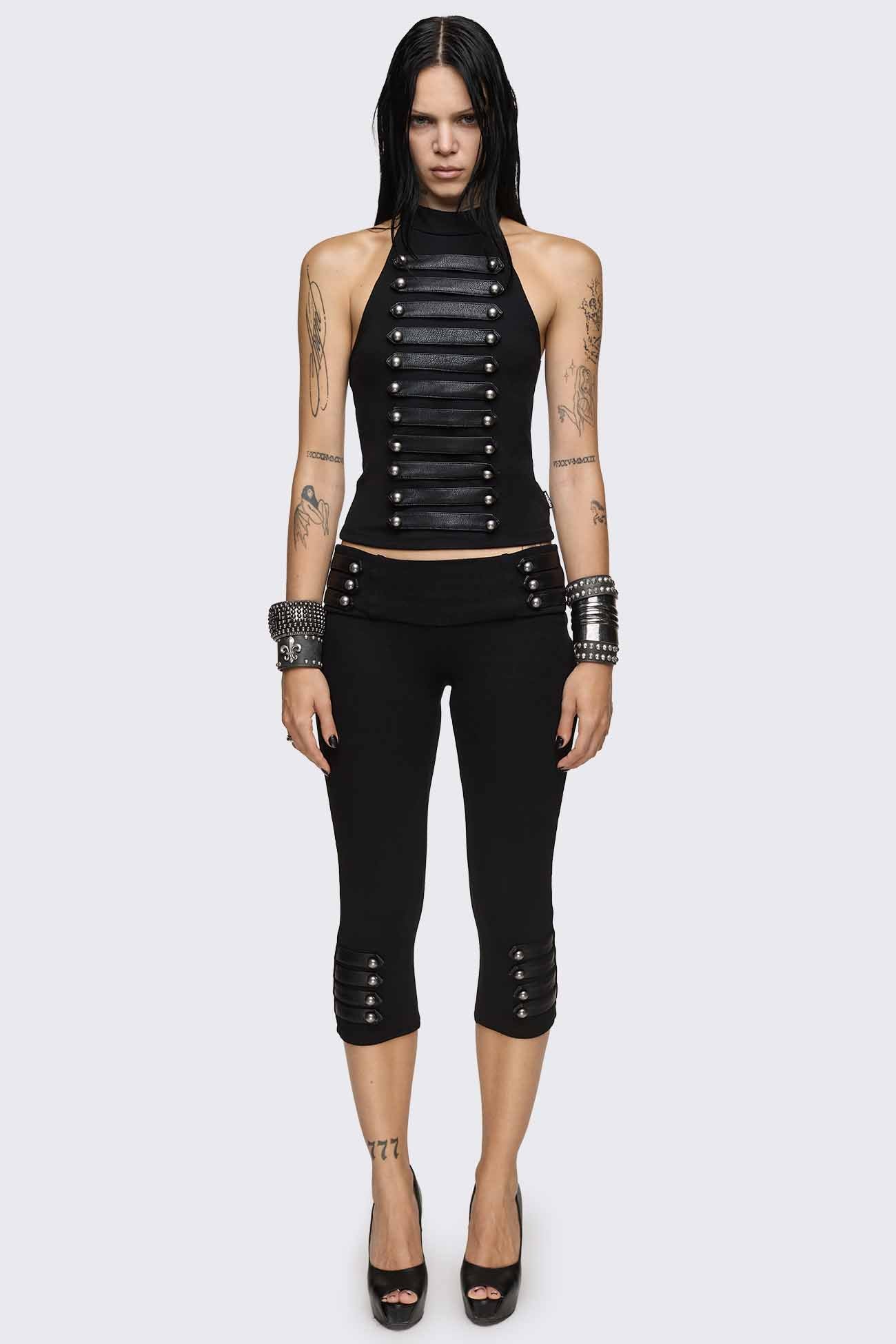 Black capri pants with strap details, silver dome buttons, ribbed waistband and slim cropped fit.
