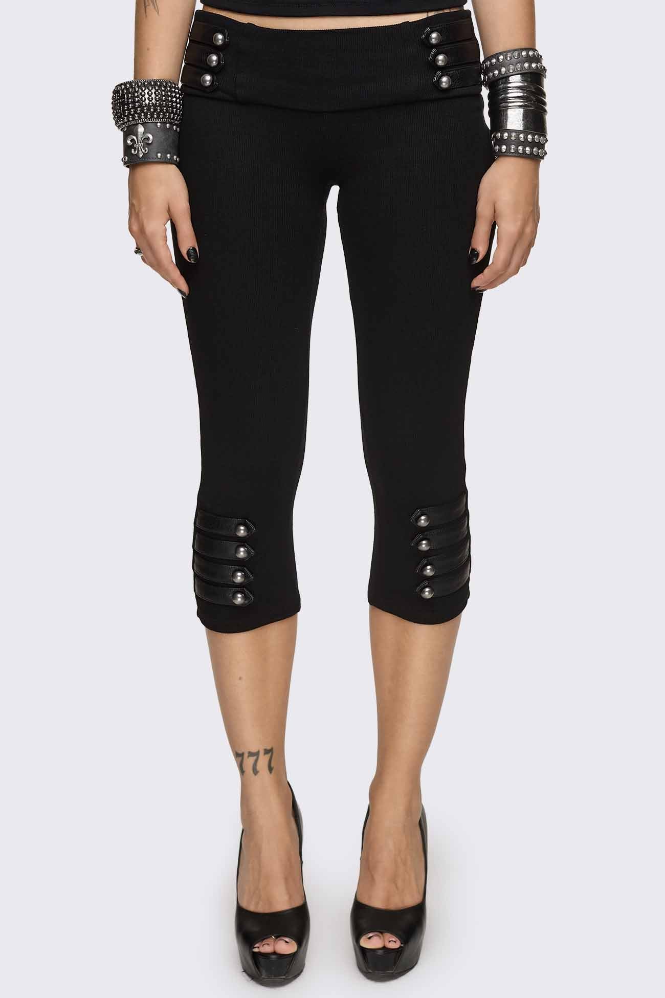 Black capri pants with strap details, silver dome buttons, ribbed waistband and slim cropped fit.