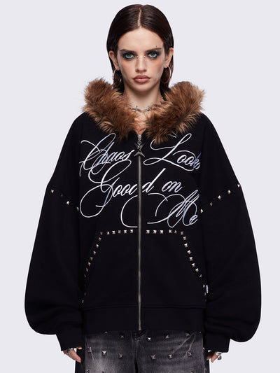 Black zip up hoodie jacket featuring a brown faux fur hood, "Chaos looks good on me" graphic embroidery and stud details.