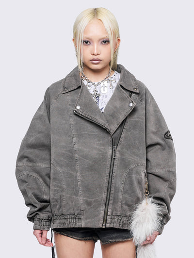 Taupe grey washed twill bomber jacket with wide lapel collar, asymmetric zip closure, oversized fit, and seam details. Features an elasticated hem, cuffs, side pockets, and an embroidered sleeve patch.