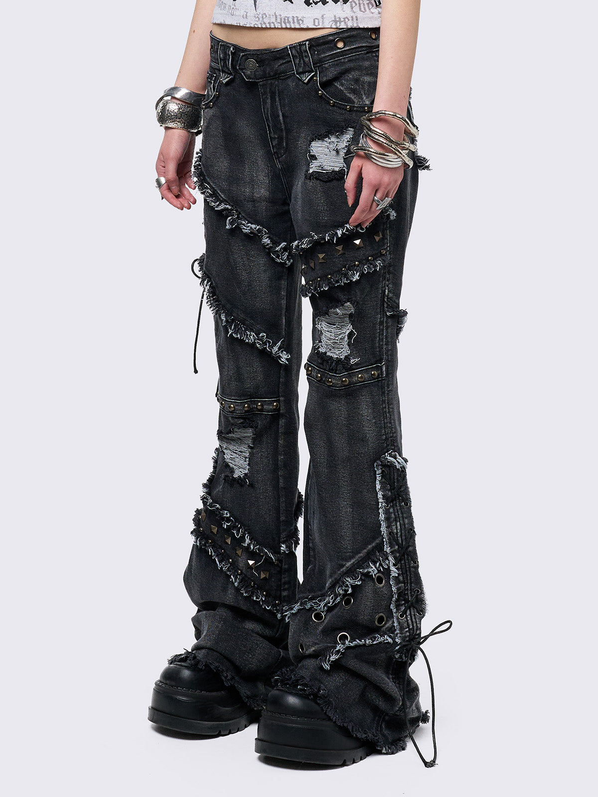 Black washed flare jeans with stud, eyelet, lace-up, and distressed details. Grunge-inspired look.