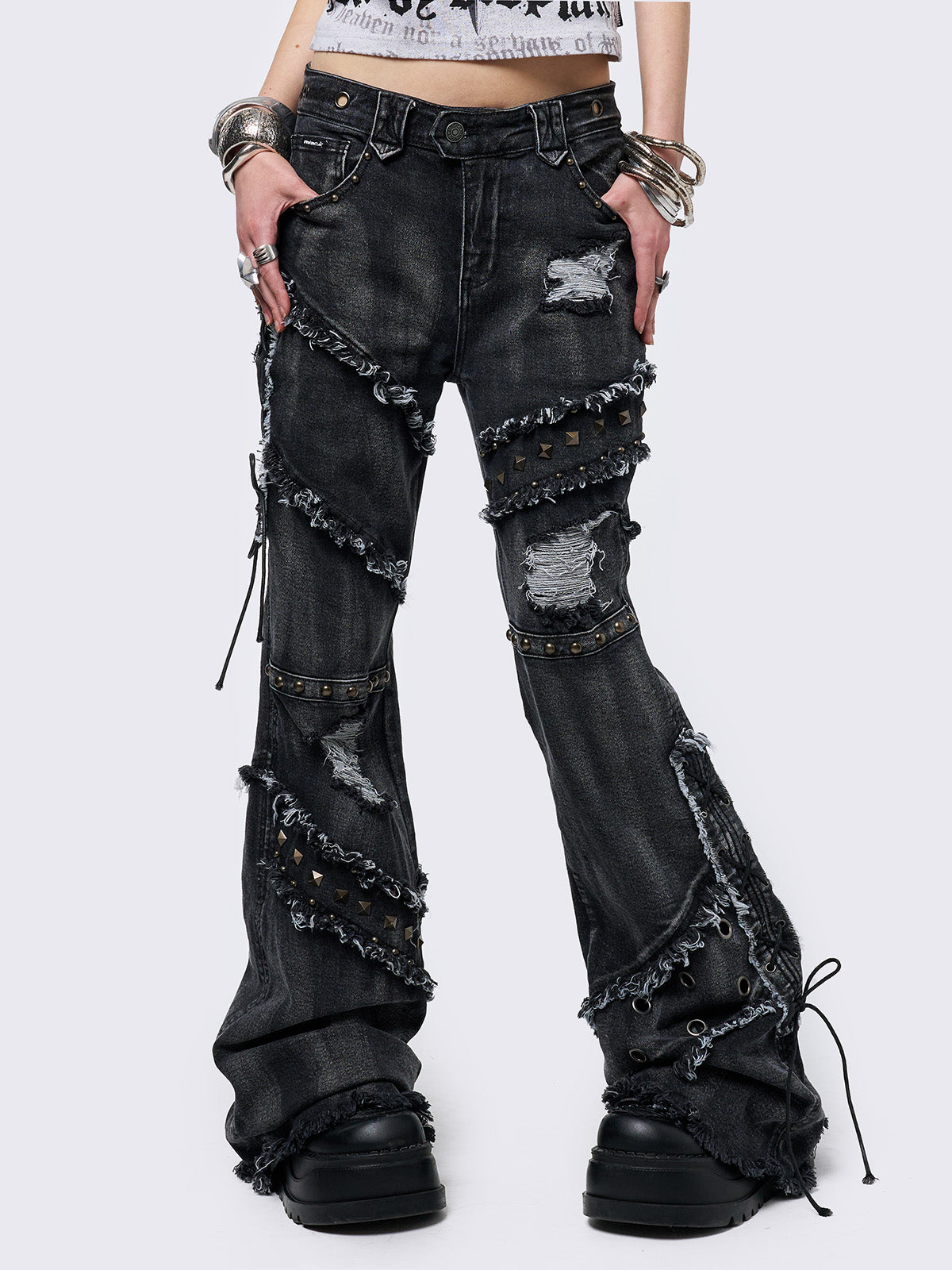 Black washed flare jeans with stud, eyelet, lace-up, and distressed details. Grunge-inspired look.