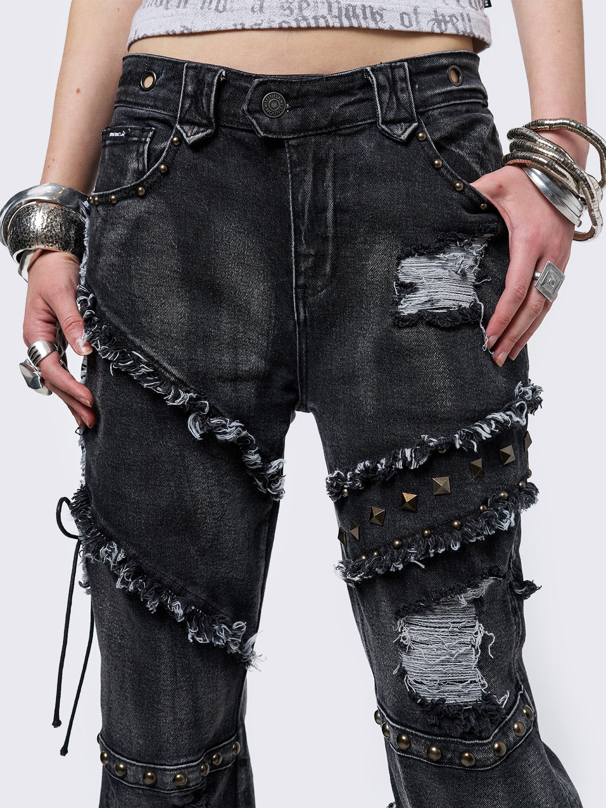 Black washed flare jeans with stud, eyelet, lace-up, and distressed details. Grunge-inspired look.