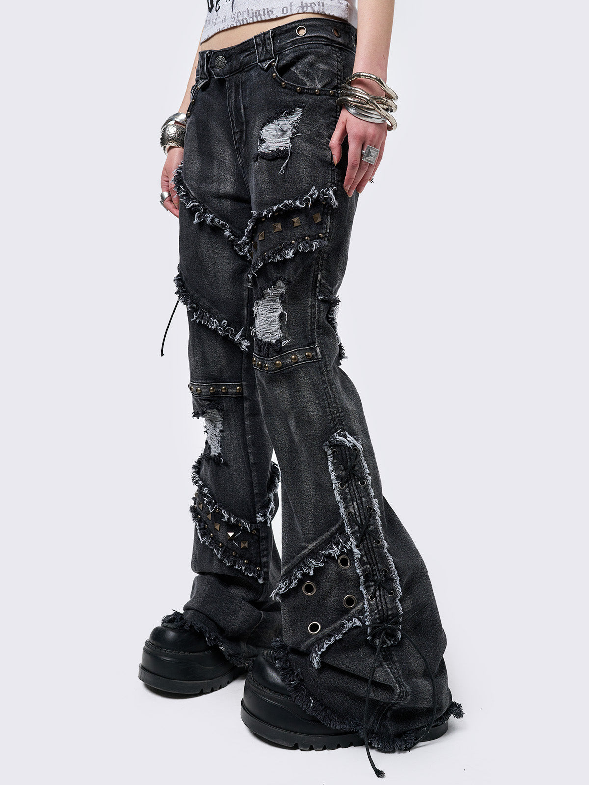 Black washed flare jeans with stud, eyelet, lace-up, and distressed details. Grunge-inspired look.