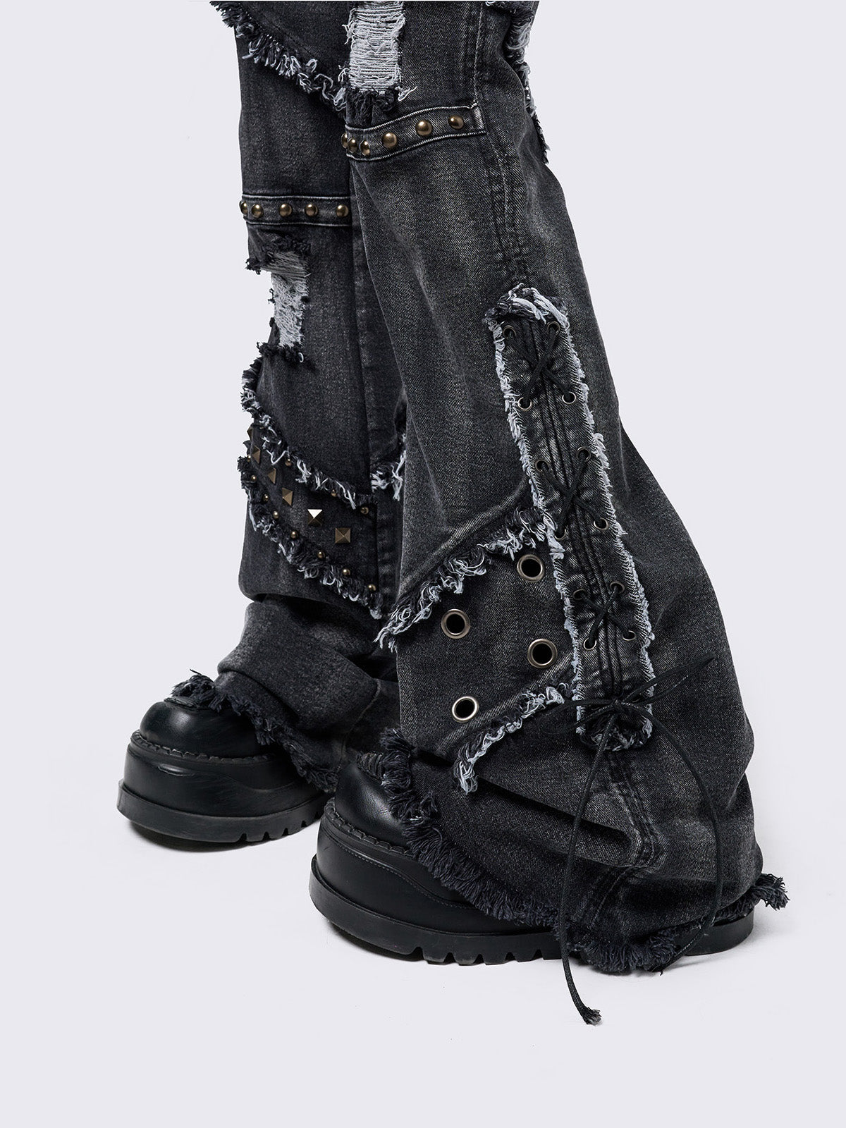 Black washed flare jeans with stud, eyelet, lace-up, and distressed details. Grunge-inspired look.