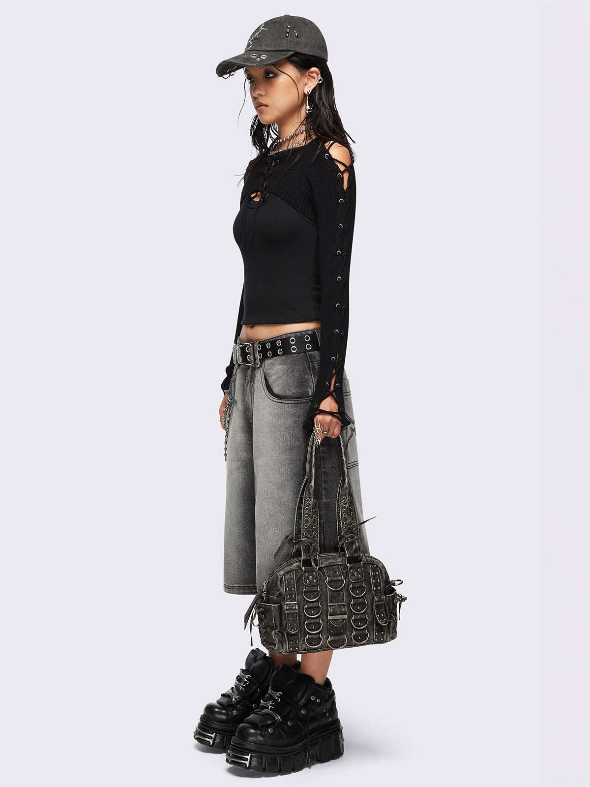 Black washed faux leather shoulder bag with multiple D-rings, buckles and hardware details, worn on shoulder with lace-up strap design.