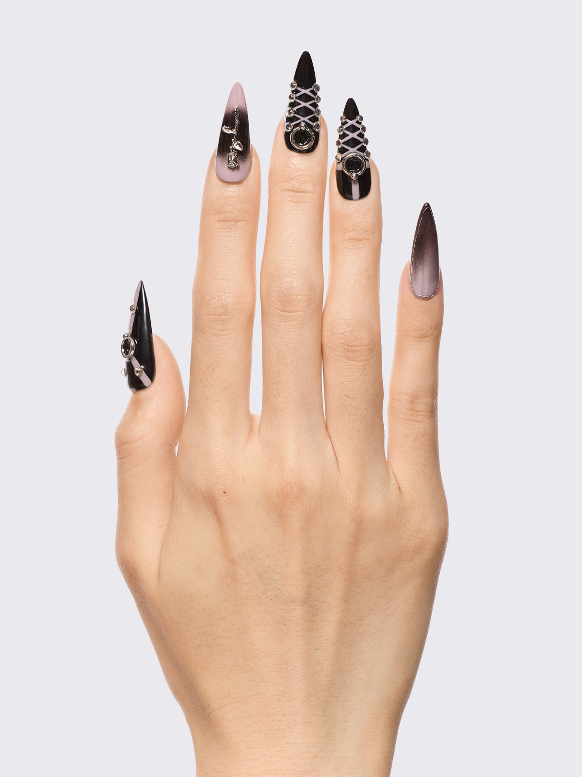 Set of stiletto press-on nails features a bold black and dusty pink ombré base, detailed with metallic piercing accents, faux corset lacing, and 3D charm embellishments. Perfect for adding edge to your outfit without a trip to the salon.
