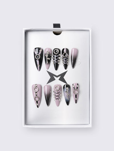 Set of stiletto press-on nails features a bold black and dusty pink ombré base, detailed with metallic piercing accents, faux corset lacing, and 3D charm embellishments. Perfect for adding edge to your outfit without a trip to the salon.