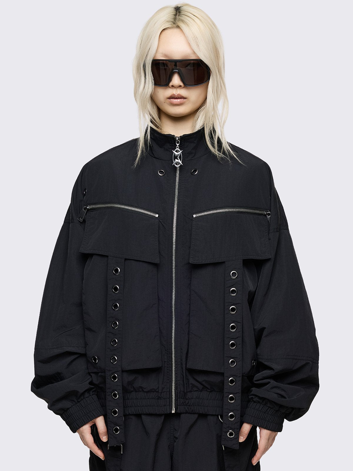 Black boxy oversized windbreaker jacket with straps and metal hardware details. 