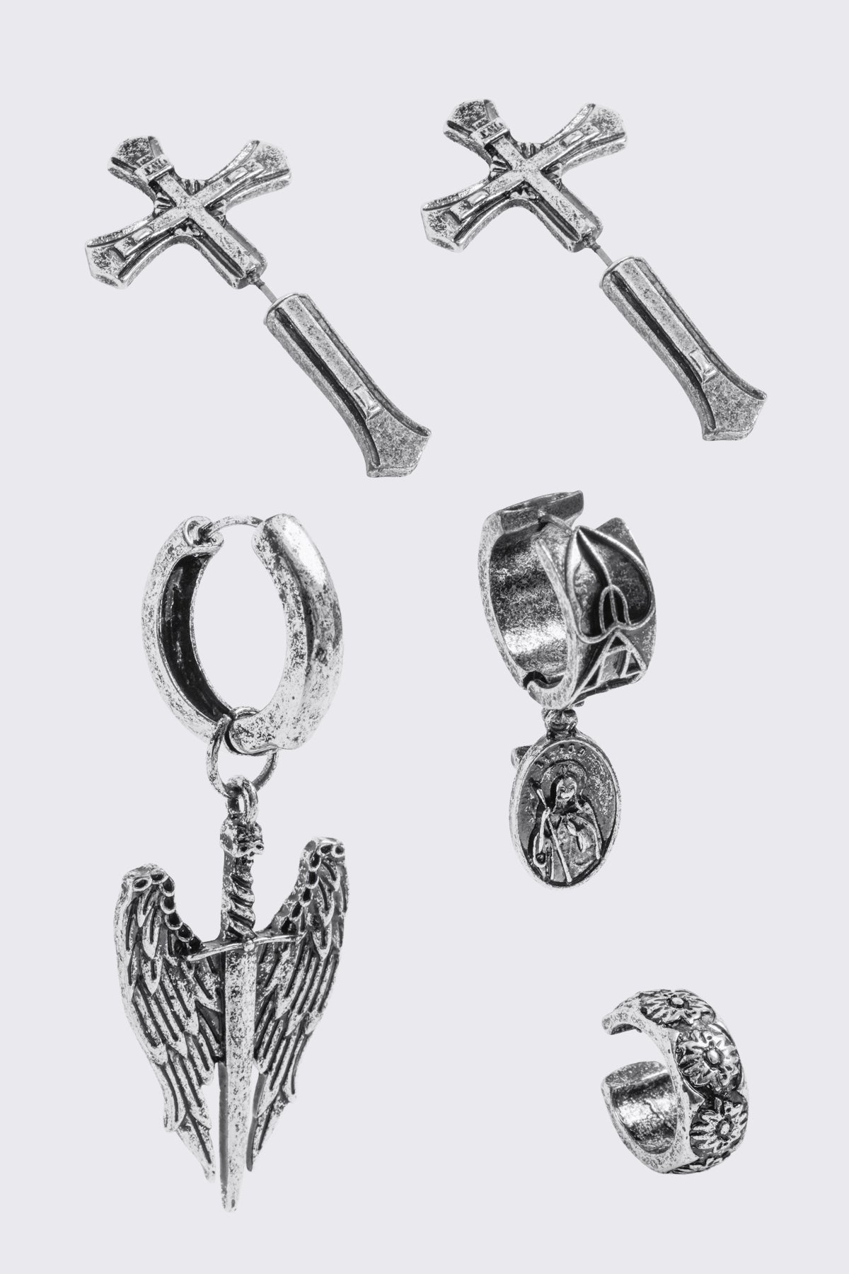 A 5-piece set of mismatched silver-toned earrings and an ear cuff featuring gothic and religious motifs, including crosses, a Virgin Mary medallion, and a winged sword dangle.