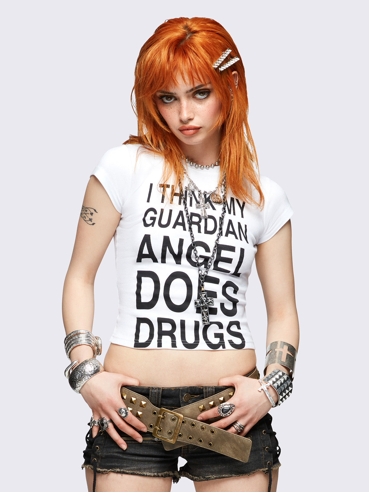 White baby tee with bold black "I think my guardian angel does drugs" front print, featuring a black cross back print.
