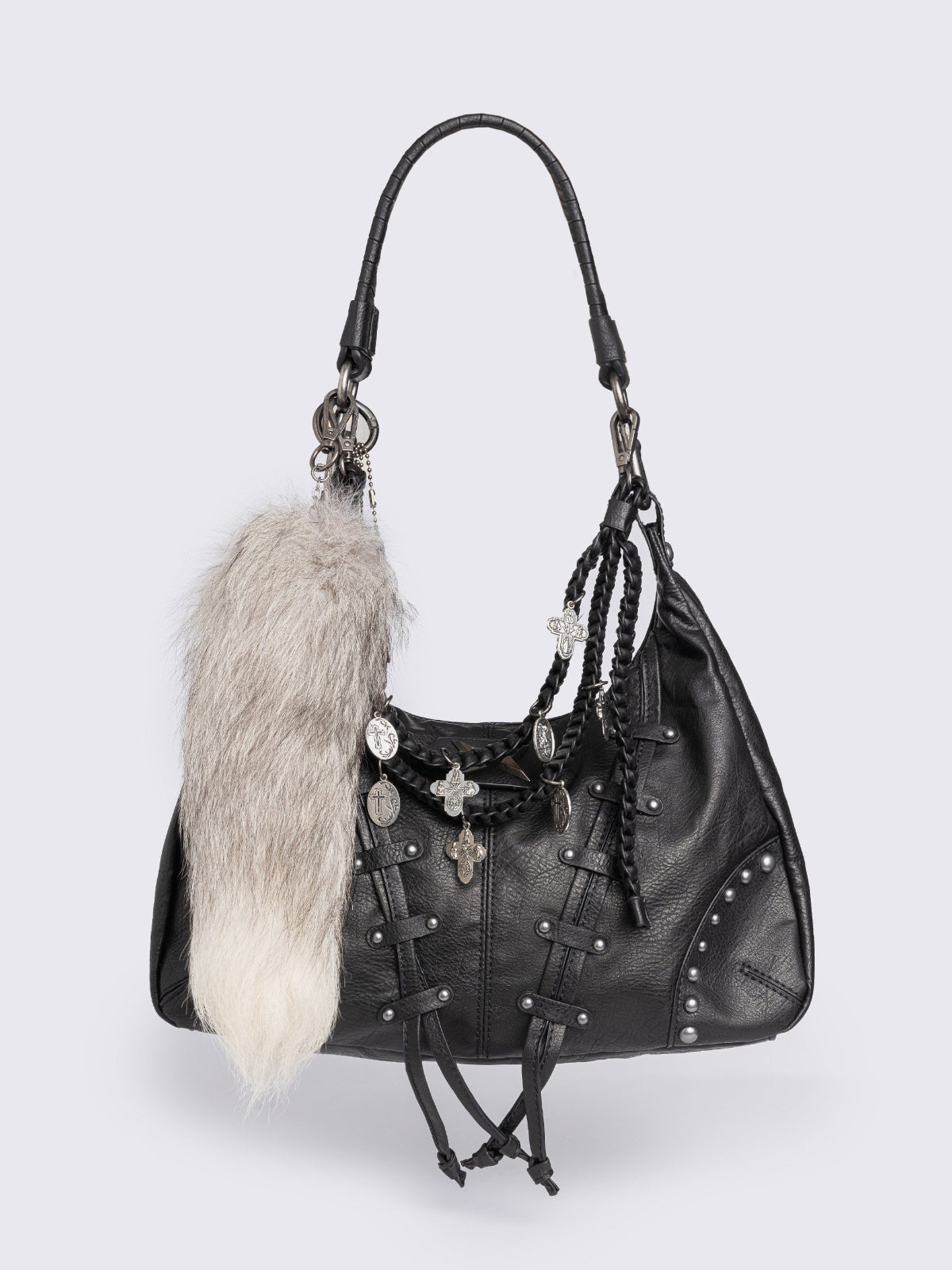 A black leather hobo bag decorated with silver studs, metallic charms, braided leather, and a large grey and white fur tail charm.