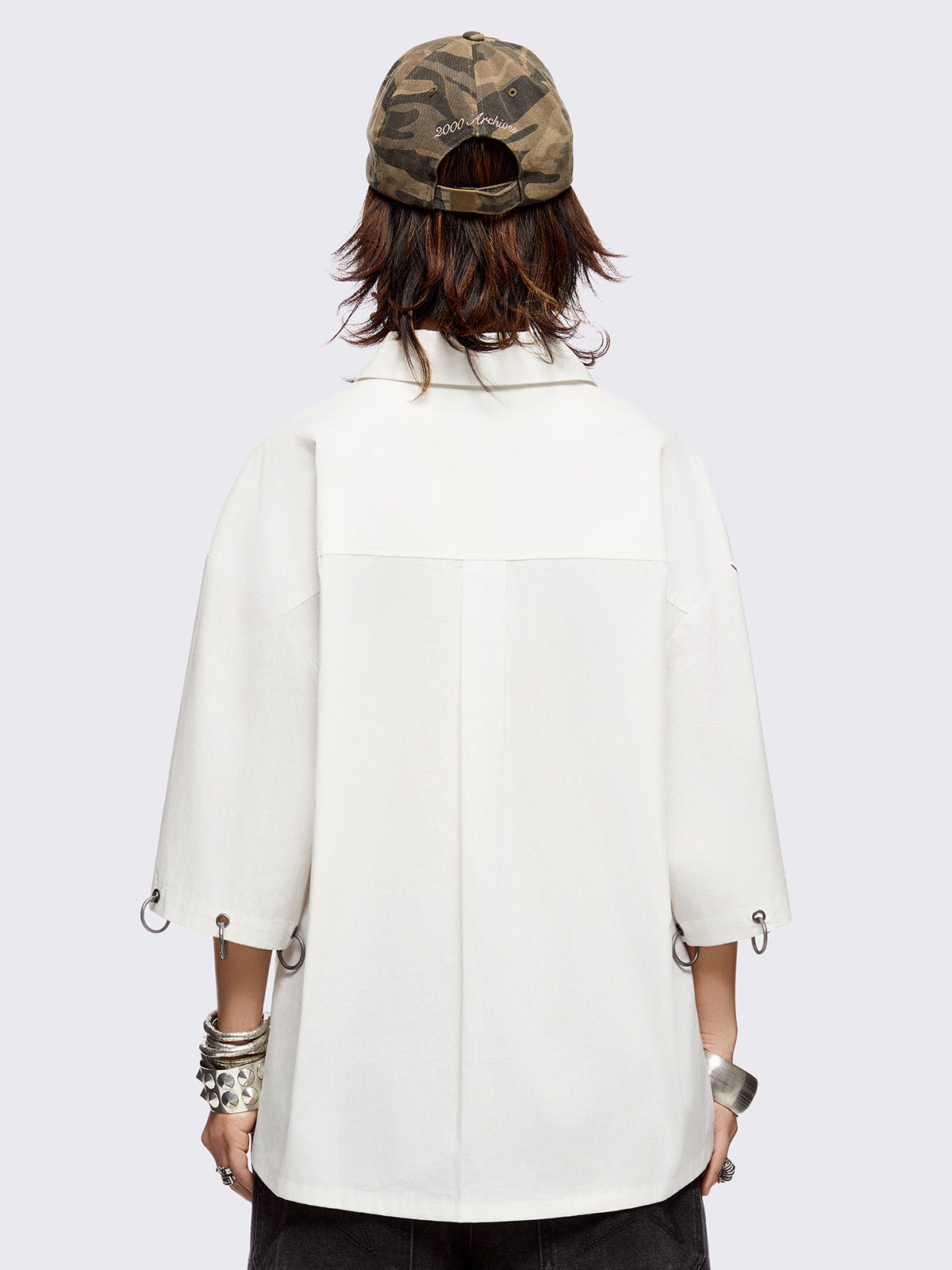 White oversized bowling shirt with black sigilism and lettering graphic print, eyelets with silver O-rings on sleeves and collar and more metal hardware details. 