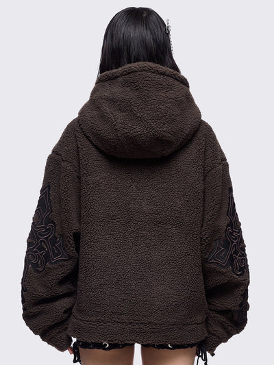 Brown fleece hoodie jacket featuring a cross patch on front and sleeves and silver stud details.