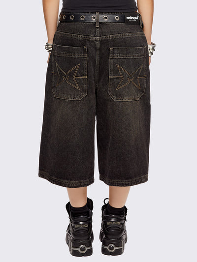 Black washed longline denim shorts with star-shaped stud and seam detail on front.